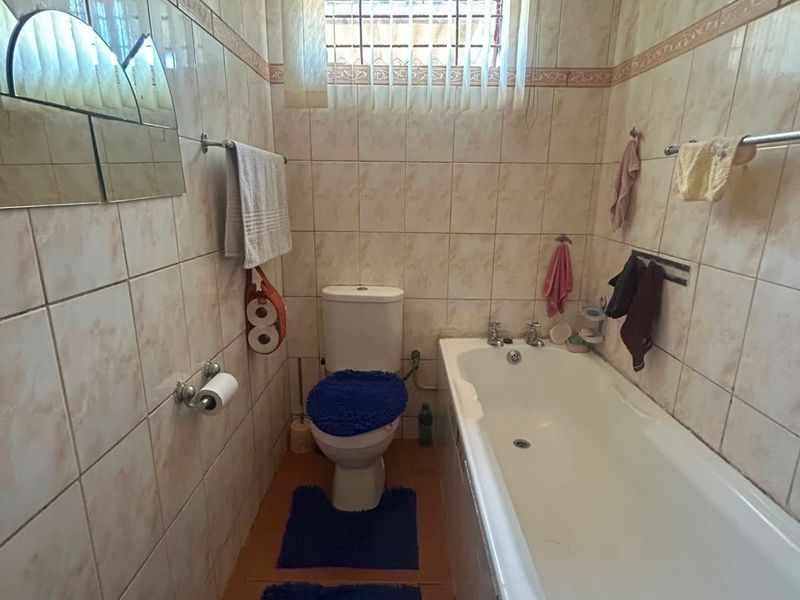 A compact bathroom featuring a standard bathtub, toilet, and full-height wall tiling. The space requires cosmetic updates to improve its dated appearance.
