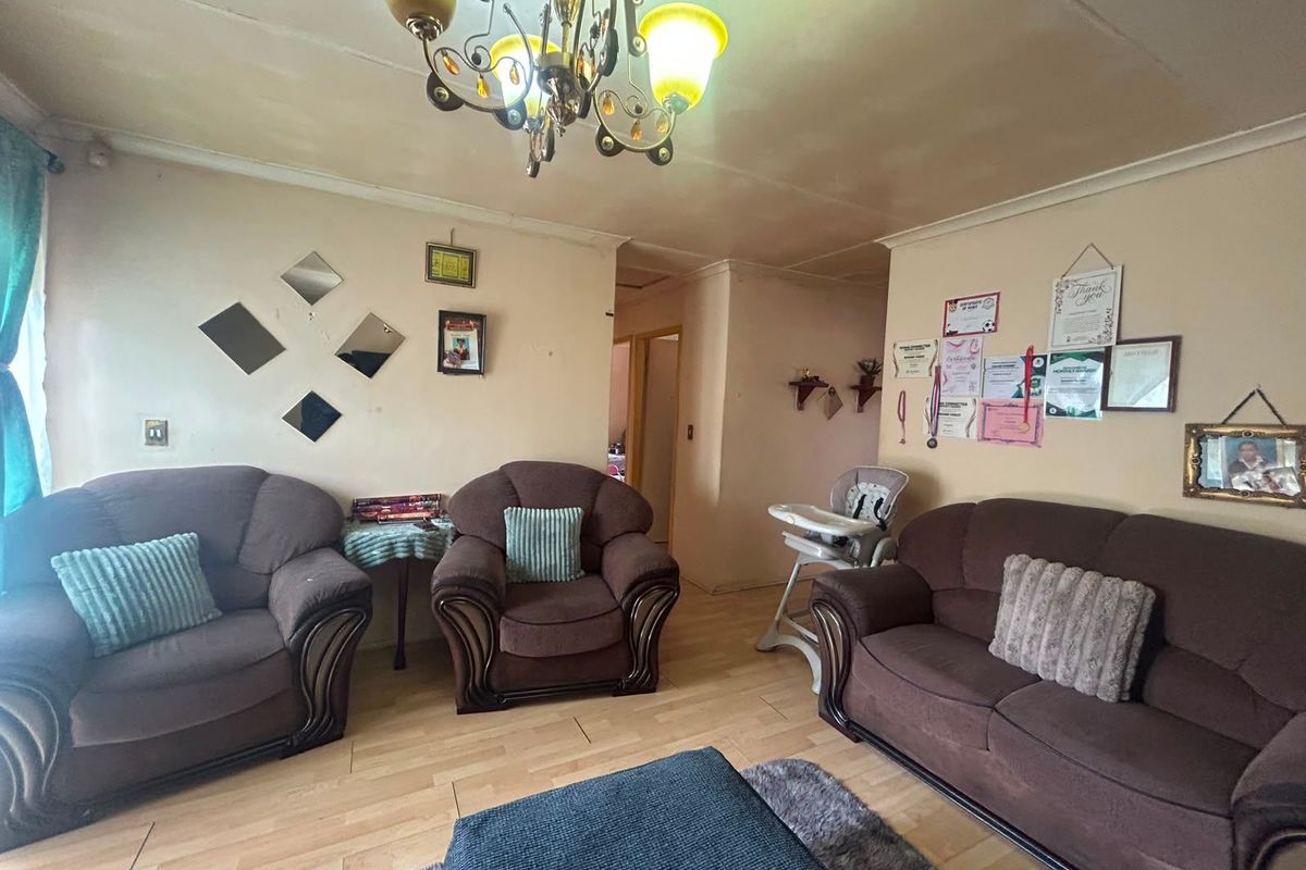 A living room featuring laminate flooring and a central chandelier, currently showing signs of wear on the ceiling and walls.
