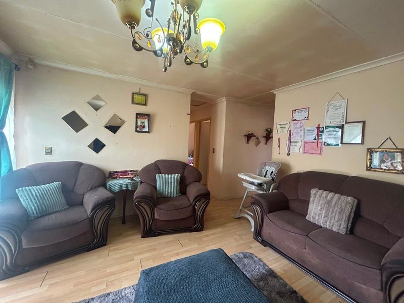 A living room featuring laminate flooring and a central chandelier, currently showing signs of wear on the ceiling and walls.