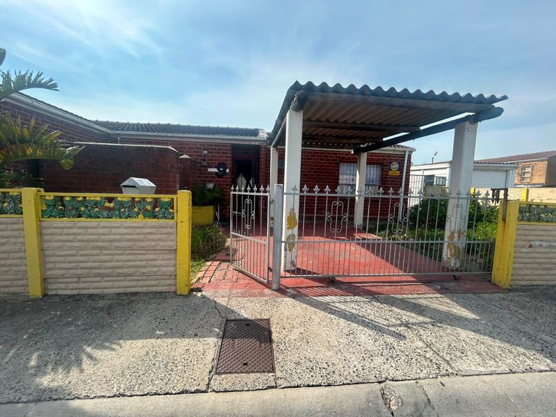 Front exterior view of a brick house featuring a gated entrance, a covered carport, and a perimeter wall.