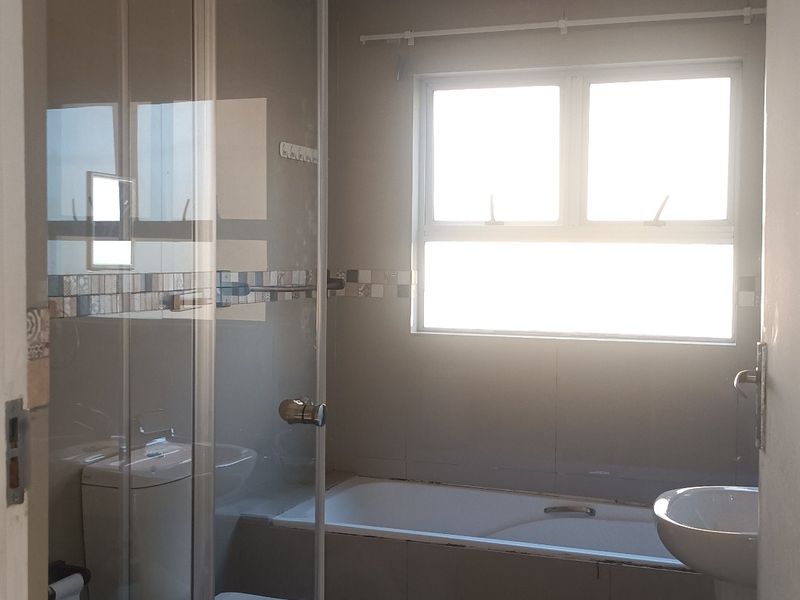 A functional bathroom featuring a shower enclosure, bathtub, pedestal basin, and toilet, with visible ceiling water staining requiring attention.