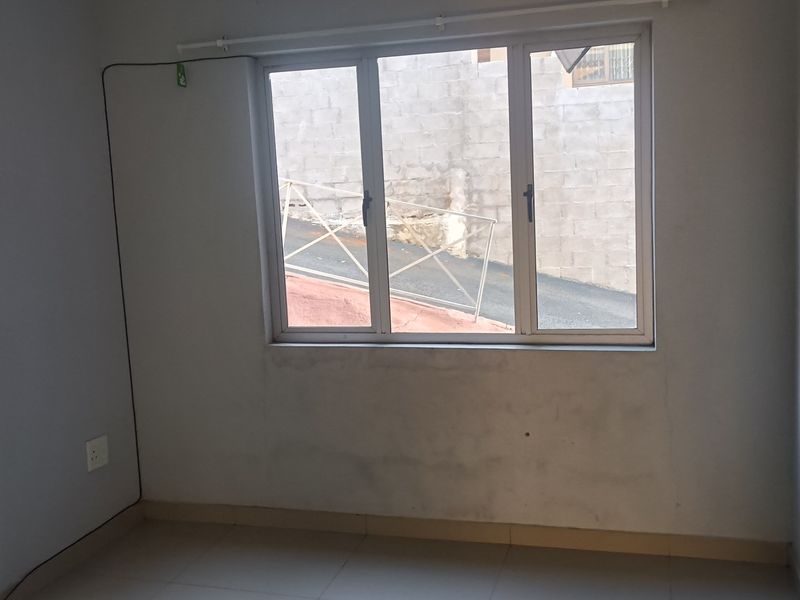 An empty bedroom featuring tiled flooring and an aluminium window frame, requiring minor cosmetic attention to the wall surfaces.