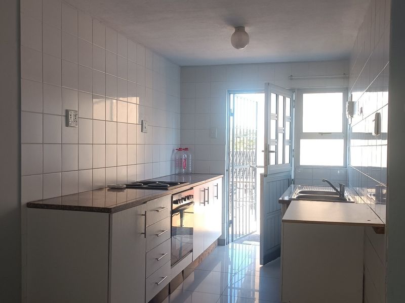 A functional, empty kitchen featuring built-in cabinetry, a built-in oven with hob, stainless steel sink, and tiled finishes with direct access to the exterior.