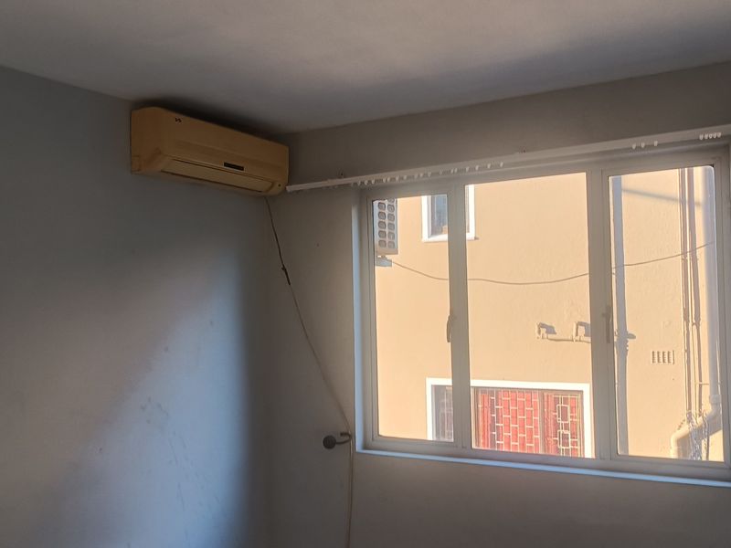 An empty bedroom featuring a wall-mounted air conditioning unit, aluminium window frames, and a curtain track, requiring minor cosmetic updates.
