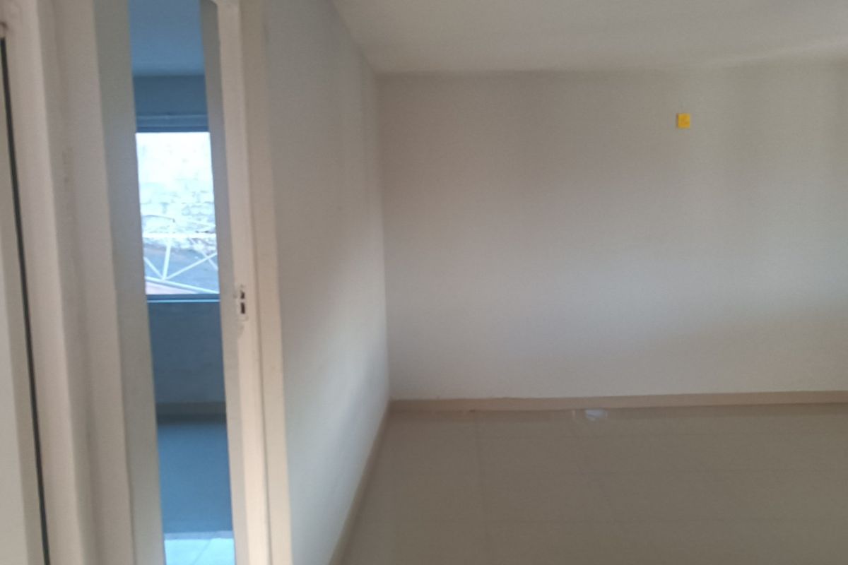 An empty, neutrally painted living area featuring tiled flooring and a doorway leading to an adjacent room.