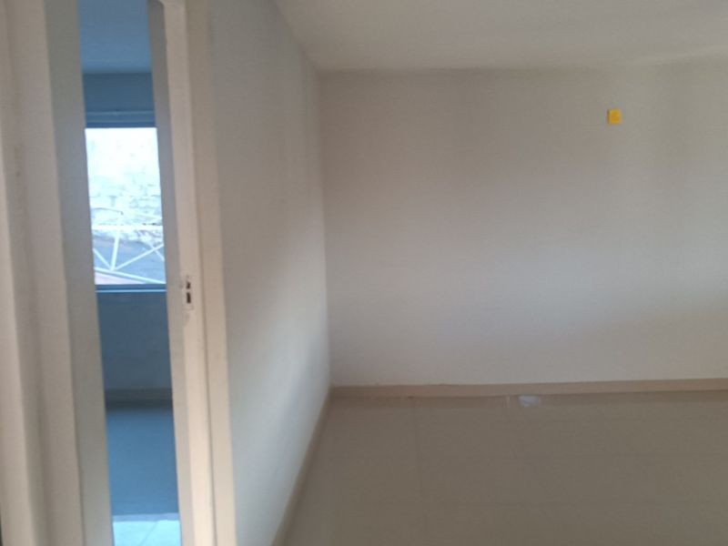 An empty, neutrally painted living area featuring tiled flooring and a doorway leading to an adjacent room.