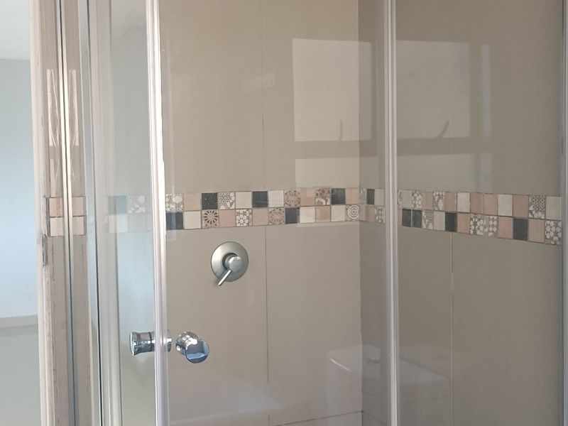 A clean, modern bathroom featuring a glass-enclosed shower with decorative mosaic floor tiling and neutral wall tiles.