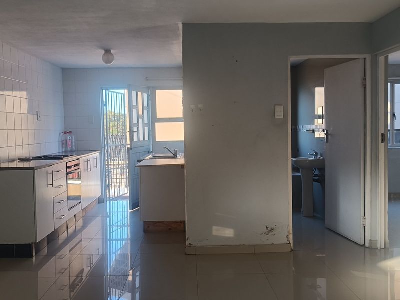 Open plan kitchen and living area featuring tiled floors, built-in cabinetry, and an adjacent bathroom with a pedestal sink.