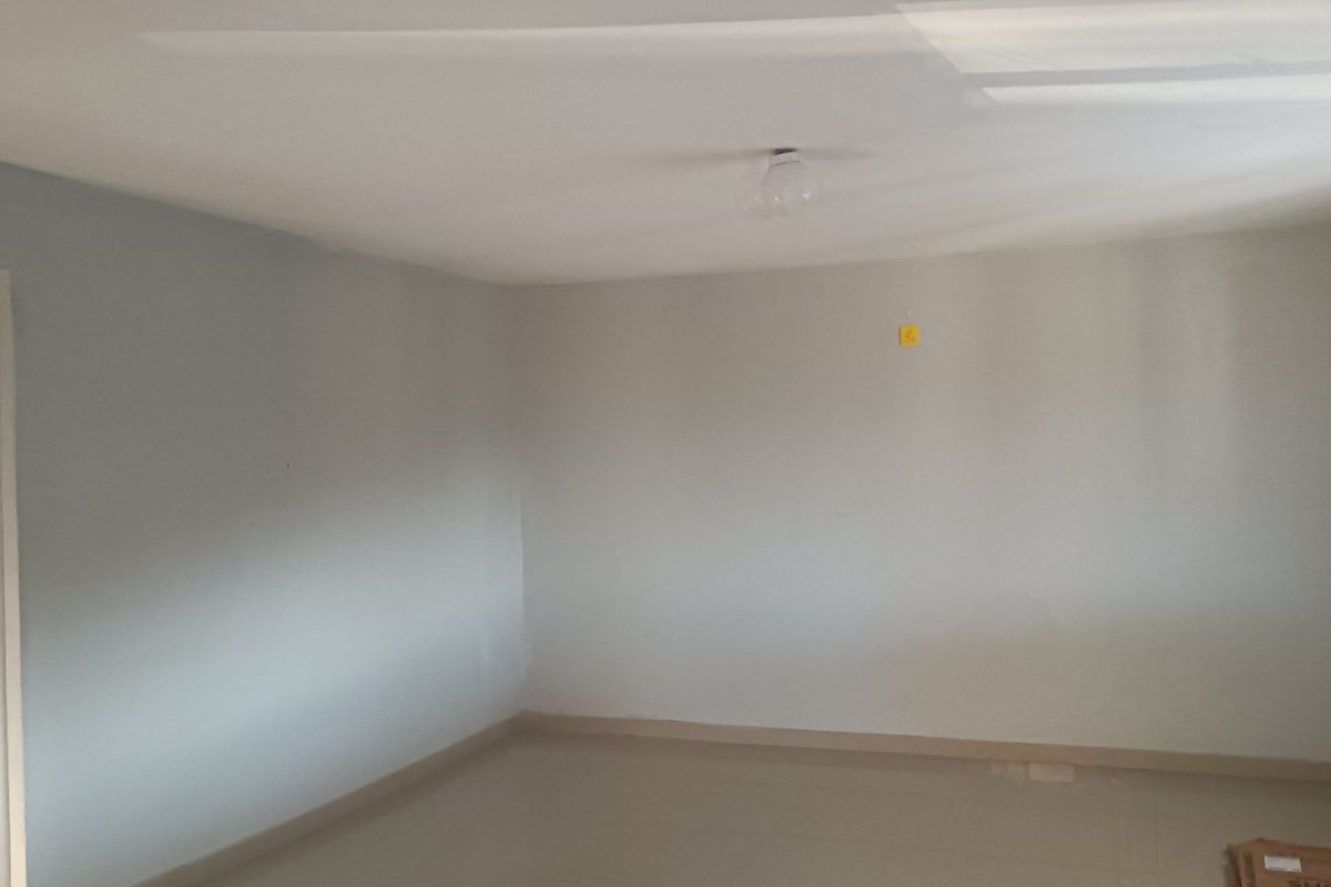 An empty, neutral-toned bedroom featuring simple finishes, a ceiling light fixture, and an electrical outlet, ready for personalization.