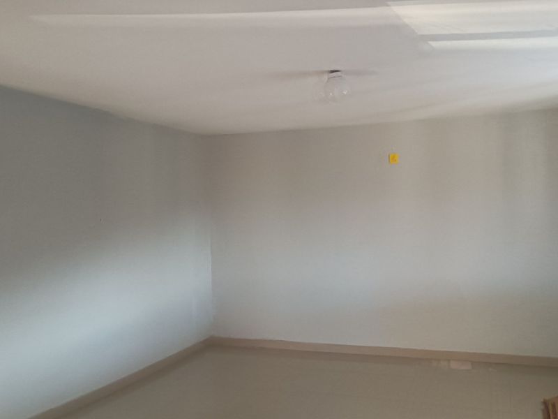 An empty, neutral-toned bedroom featuring simple finishes, a ceiling light fixture, and an electrical outlet, ready for personalization.