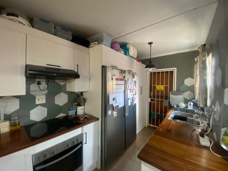 A functional kitchen featuring white cabinetry, wooden countertops, a modern electric hob, and a decorative hexagonal tiled backsplash with direct access to a security gate.