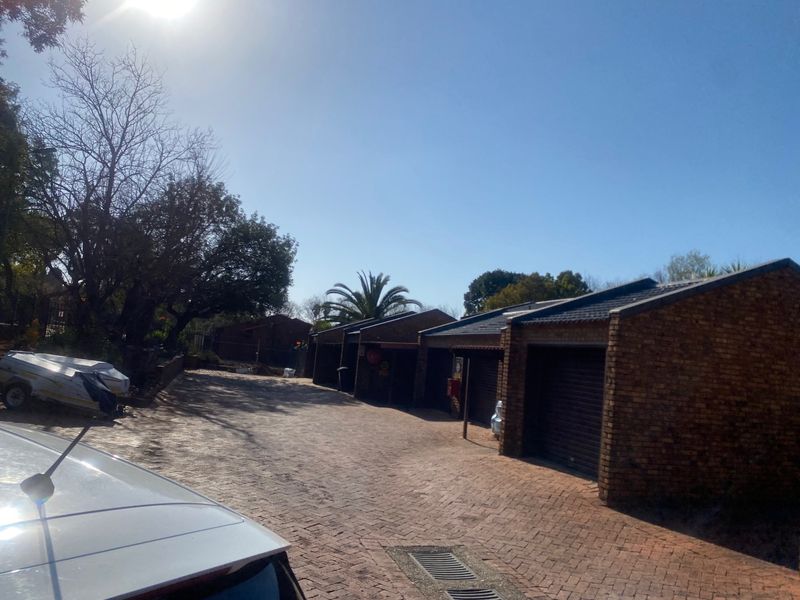 A row of brick-built garages with roller doors and a paved driveway area within the townhouse complex.