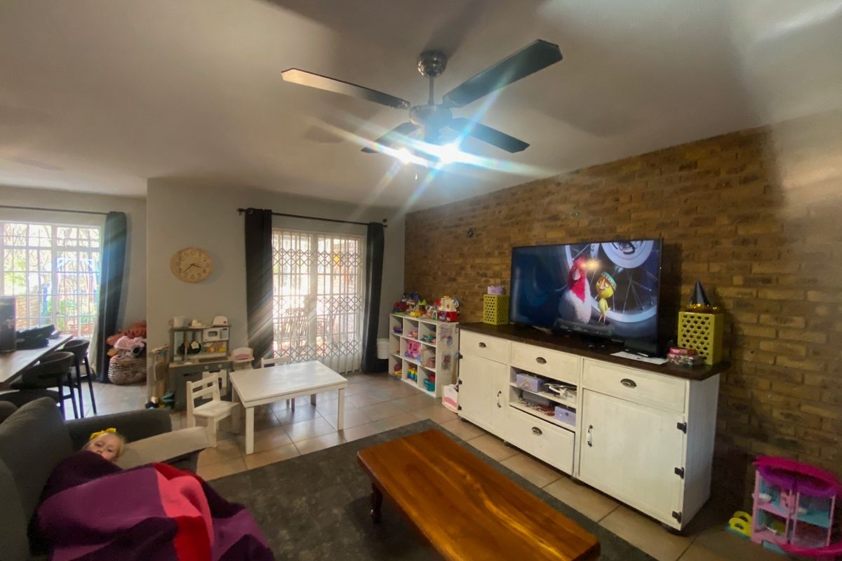 A living room featuring an exposed brick wall, tiled flooring, and a ceiling fan, with direct access to an outdoor area through a sliding door.