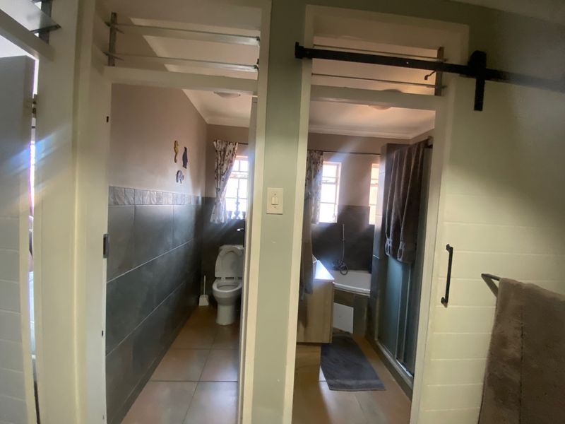 A split-layout bathroom featuring a separate toilet area and a combined bathtub and shower enclosure with tiled finishes.
