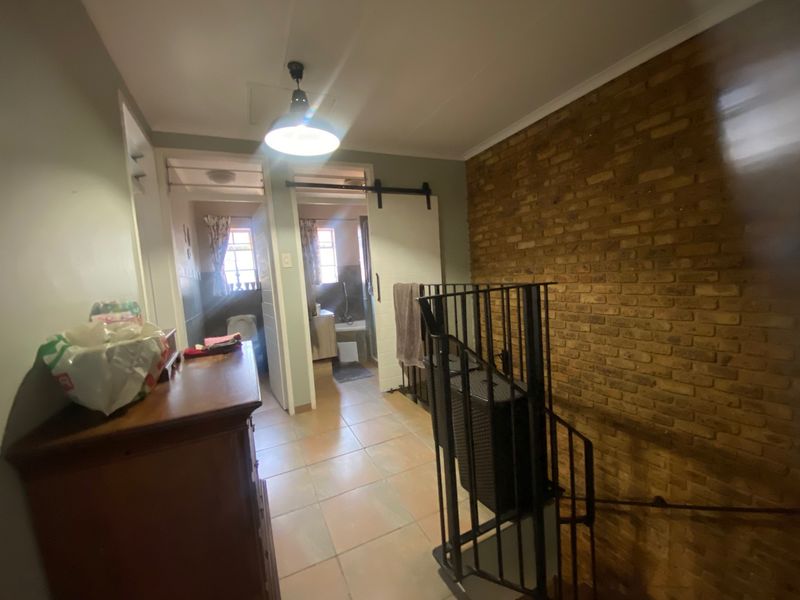 A hallway featuring an exposed brick wall, tiled flooring, and a sliding barn door leading to the bathroom area.