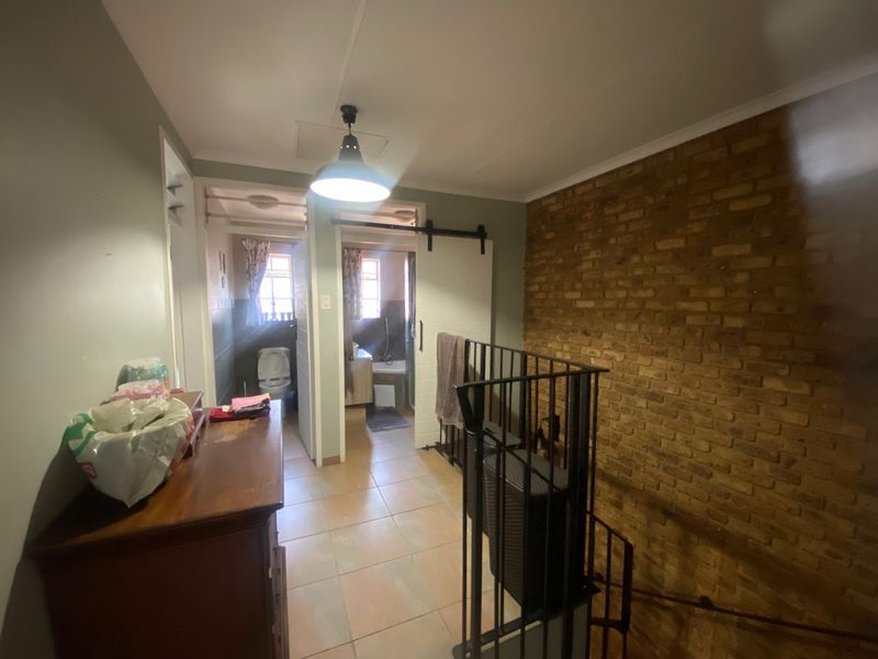 A hallway area featuring an exposed brick wall, tiled flooring, and a sliding barn door leading to the bathroom.
