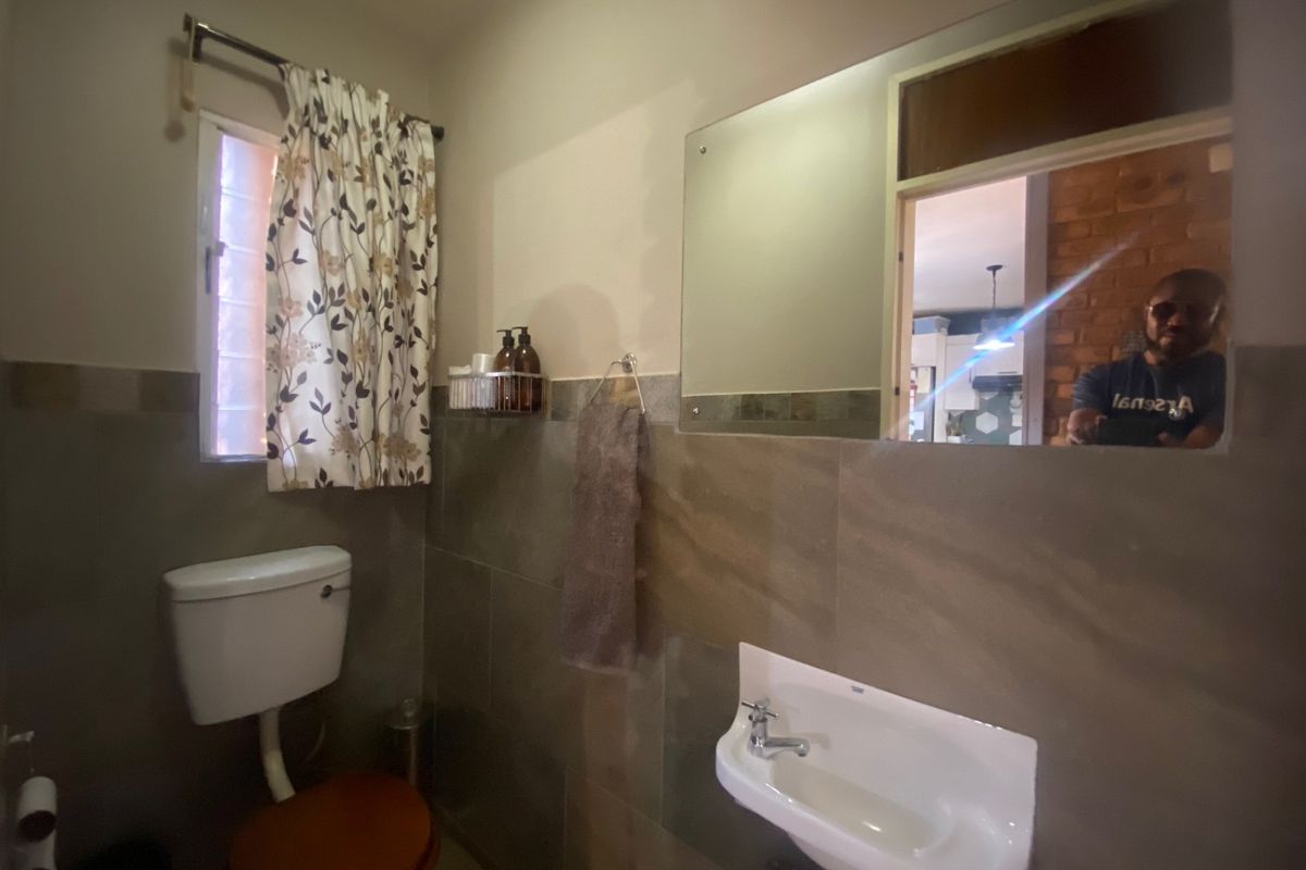 A functional bathroom featuring tiled walls, a wall-mounted basin, and a large mirror, providing essential amenities in a compact layout.