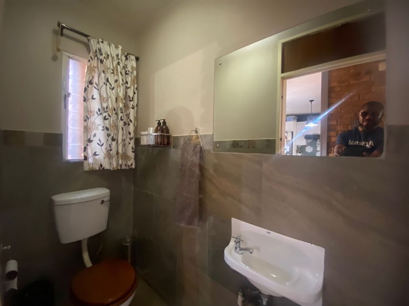 A functional bathroom featuring tiled walls, a wall-mounted basin, and a large mirror, providing essential amenities in a compact layout.