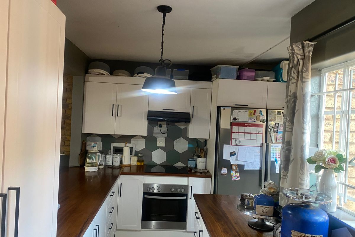 A functional kitchen featuring white cabinetry, warm wooden countertops, a hexagonal tile backsplash, and integrated appliances including an oven and hob.