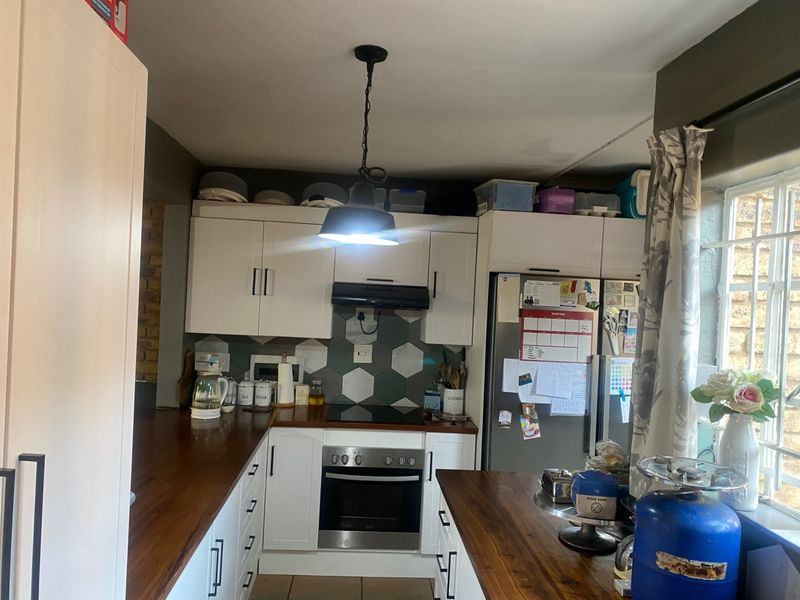 A functional kitchen featuring white cabinetry, warm wooden countertops, a hexagonal tile backsplash, and integrated appliances including an oven and hob.