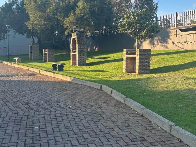 A well-maintained communal garden area featuring brick paving, landscaped lawn, and multiple built-in brick braai facilities.