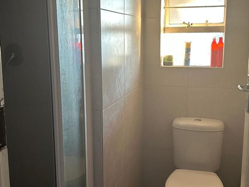 A compact bathroom featuring a shower enclosure, a standard toilet, and neutral wall tiling with a window for natural light.