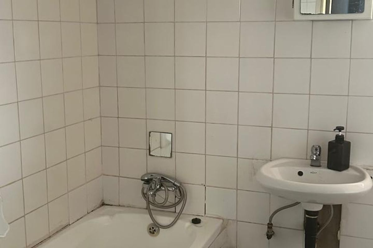 A dated bathroom featuring a bathtub, wall-mounted basin, and tiled finishes, currently requiring maintenance and cosmetic updates to improve its overall condition.