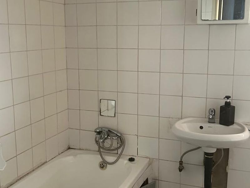 A dated bathroom featuring a bathtub, wall-mounted basin, and tiled finishes, currently requiring maintenance and cosmetic updates to improve its overall condition.
