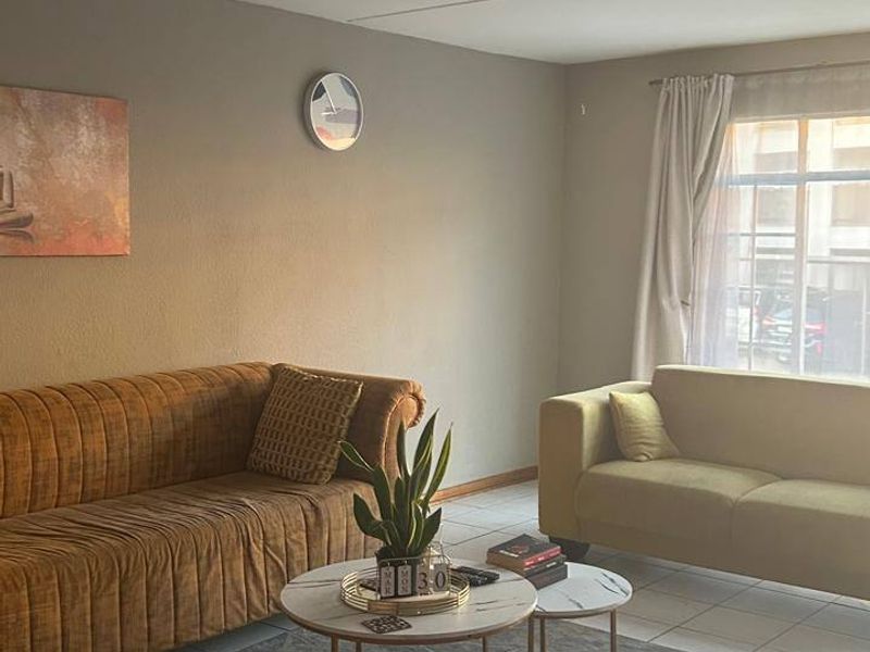 A comfortable living room featuring tiled flooring, neutral wall tones, and natural light from a large window.