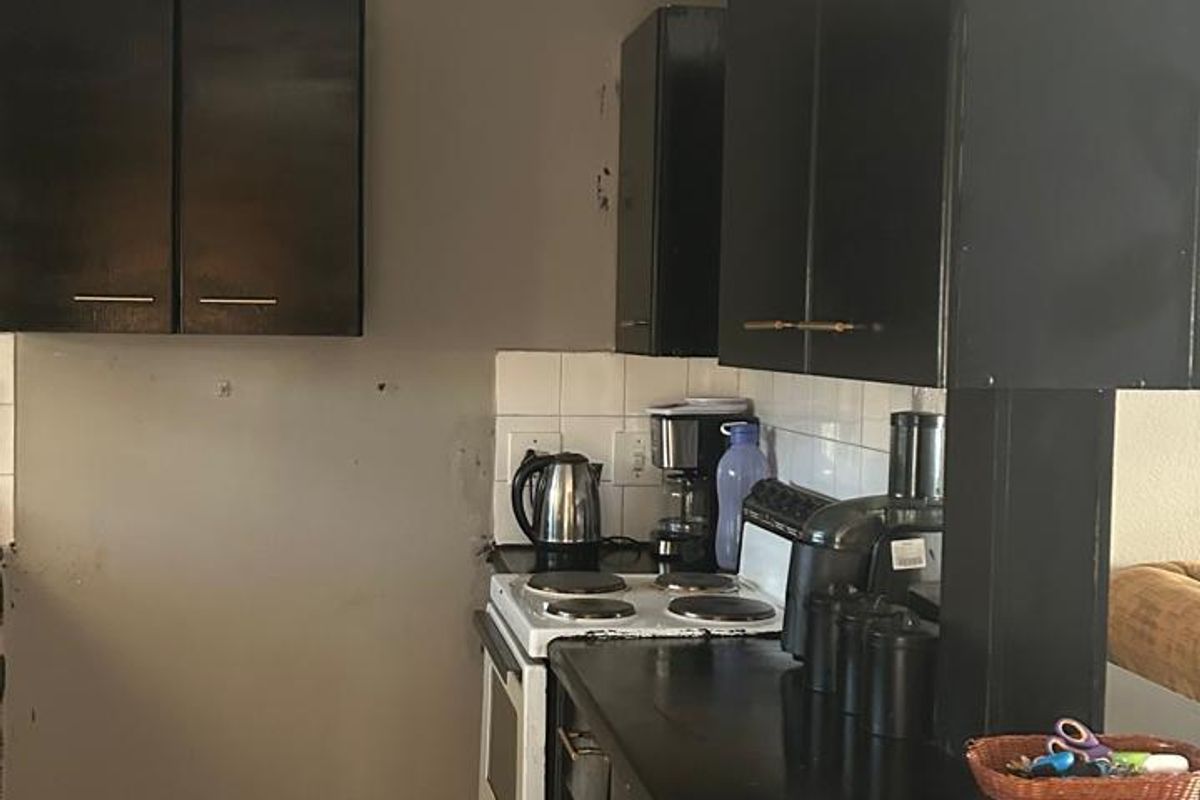 A compact kitchen featuring dark built-in cabinetry, a white electric stove, tiled backsplash, and tiled flooring, offering potential for a modern renovation.