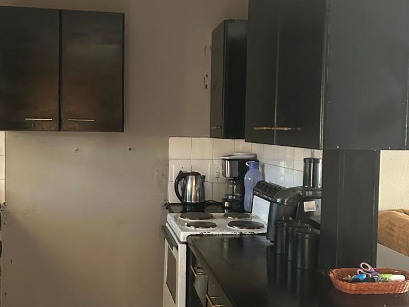 A compact kitchen featuring dark built-in cabinetry, a white electric stove, tiled backsplash, and tiled flooring, offering potential for a modern renovation.