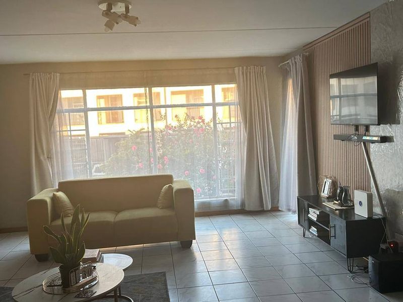 A living room featuring tiled flooring and a decorative slatted wood feature wall, with large windows providing natural light.