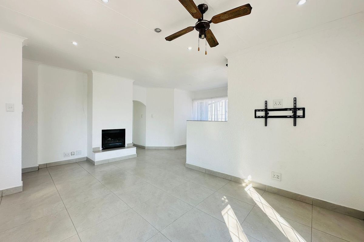 Spacious, light-filled living room featuring neutral tiled flooring, a built-in fireplace, ceiling fan, and recessed lighting, offering a clean, blank canvas for interior design.