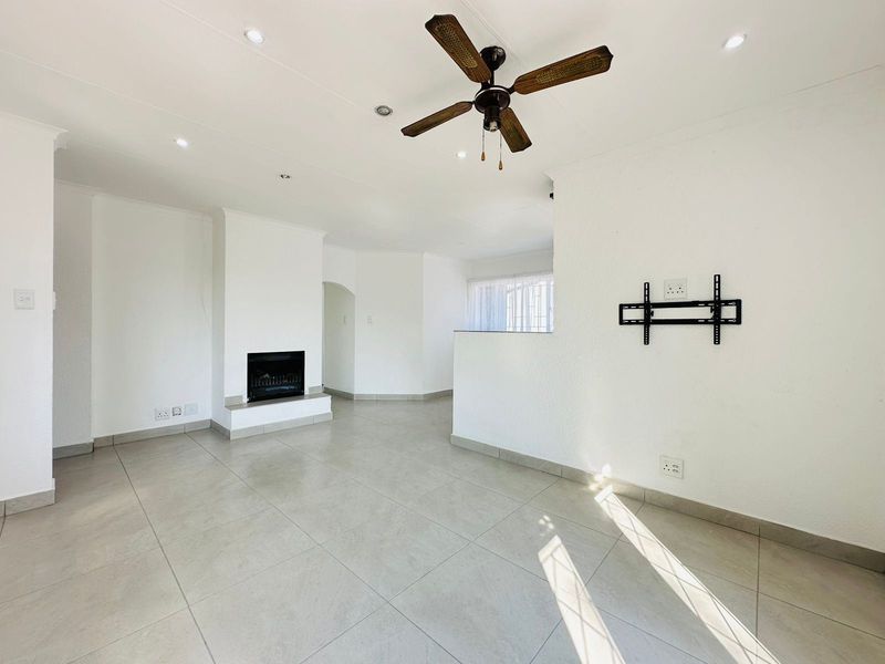 Spacious, light-filled living room featuring neutral tiled flooring, a built-in fireplace, ceiling fan, and recessed lighting, offering a clean, blank canvas for interior design.