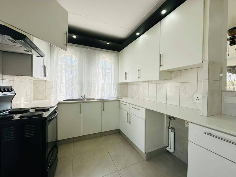 A clean, functional kitchen featuring white built-in cabinetry, tiled backsplash, stainless steel sink, and recessed lighting, providing a bright and practical workspace.