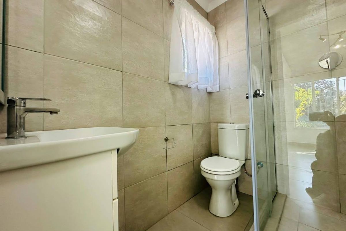 A clean, modern bathroom featuring neutral wall tiles, a vanity basin with chrome mixer, a ceramic toilet, and a glass-enclosed shower.