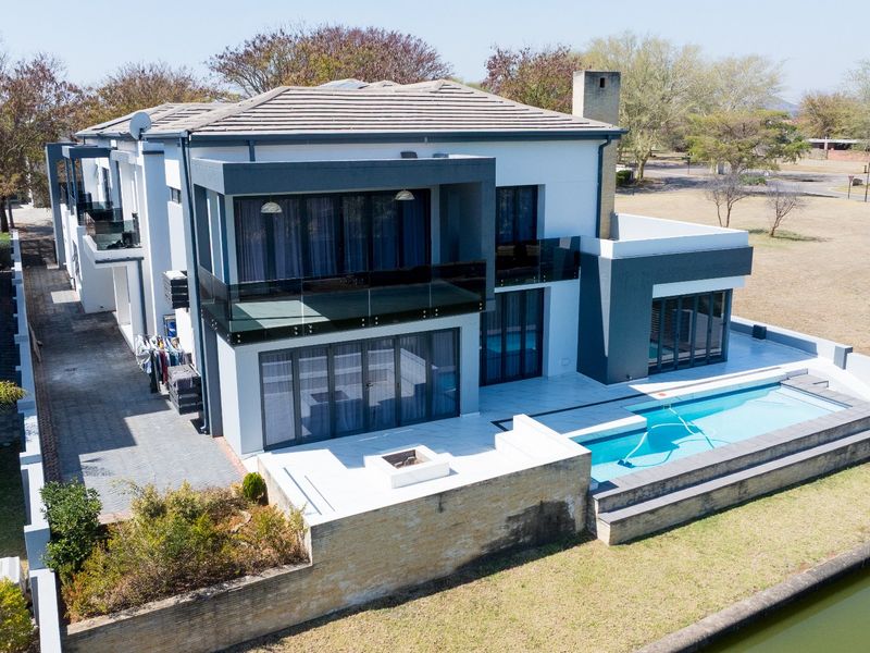 Aerial view of a modern double-story residence featuring a swimming pool, tiled patio with built-in fire pit, and glass balcony balustrades.