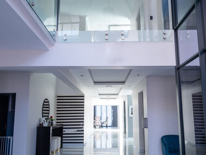 Spacious double-volume entrance hall featuring polished porcelain floor tiles, a modern glass balustrade, and contemporary architectural design elements.