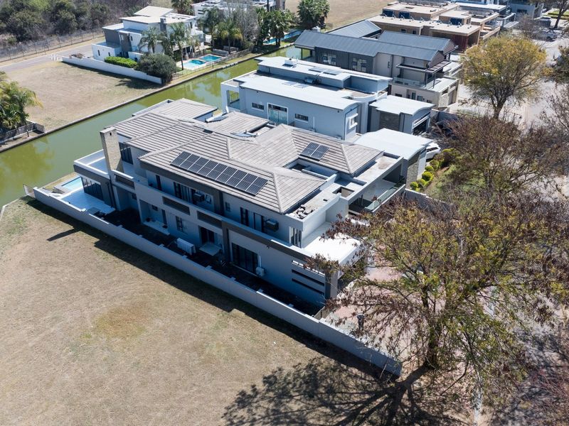 Aerial view of a modern multi-story residence featuring a tiled roof with integrated solar panels, a private swimming pool, and direct canal frontage.