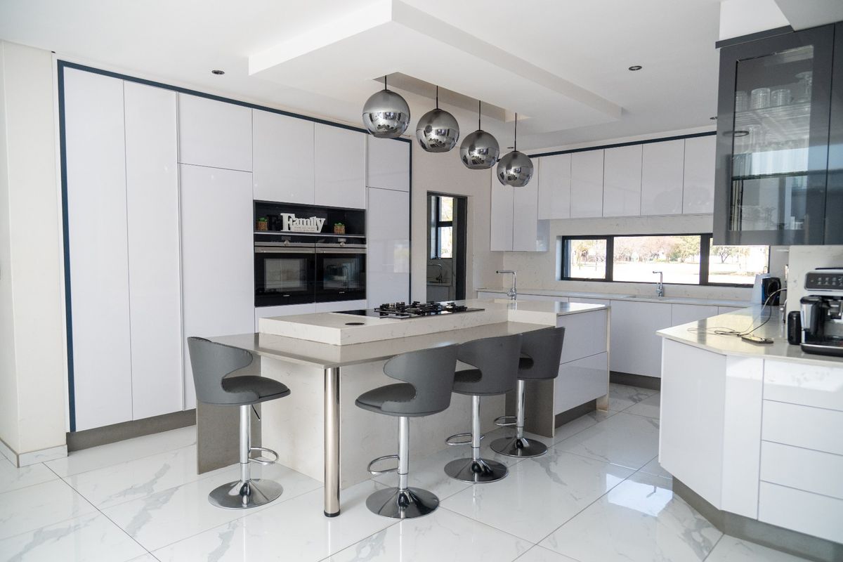 Modern, high-end kitchen featuring a large central island with integrated gas cooktop, sleek white cabinetry, double built-in ovens, and polished marble-look floor tiles.