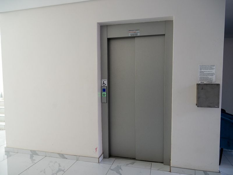 A clean, modern hallway featuring a built-in elevator with accessibility controls and polished marble-look tiled flooring.