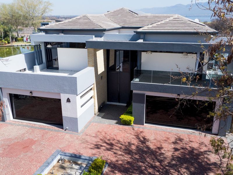 Modern double-story residence featuring a paved driveway, double garage, and upper-level balcony with glass balustrades, set in a well-maintained estate environment.