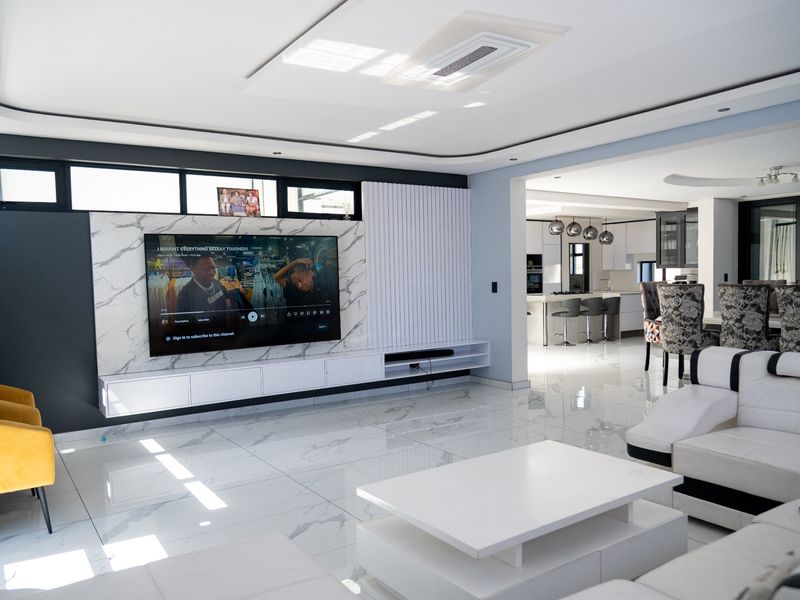Spacious open-plan living and kitchen area featuring high-end marble-look floor tiles, a modern built-in media wall, and contemporary kitchen cabinetry.