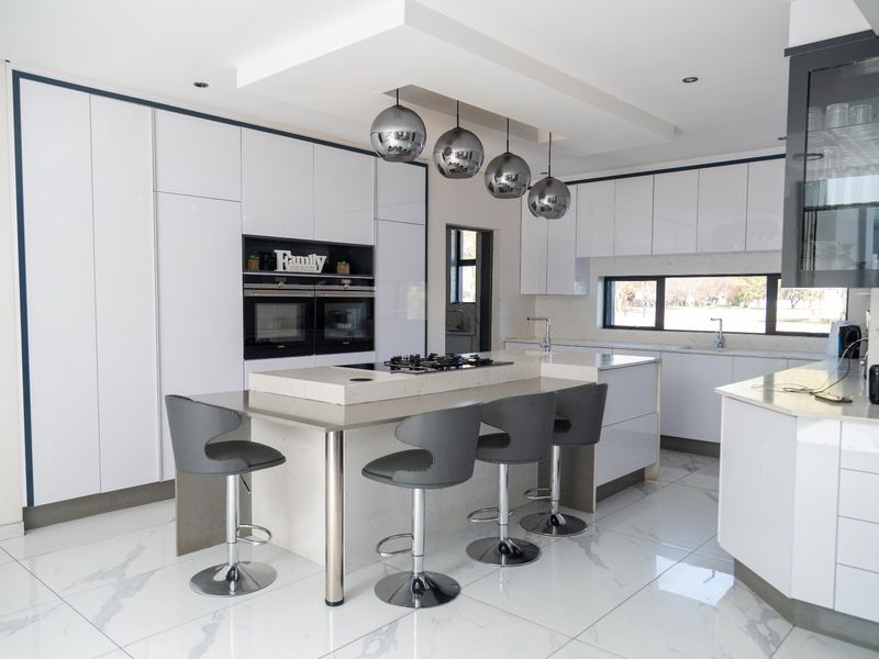 Modern, high-end kitchen featuring a large central island with integrated gas cooktop, sleek white cabinetry, double built-in ovens, and polished marble-look floor tiles.