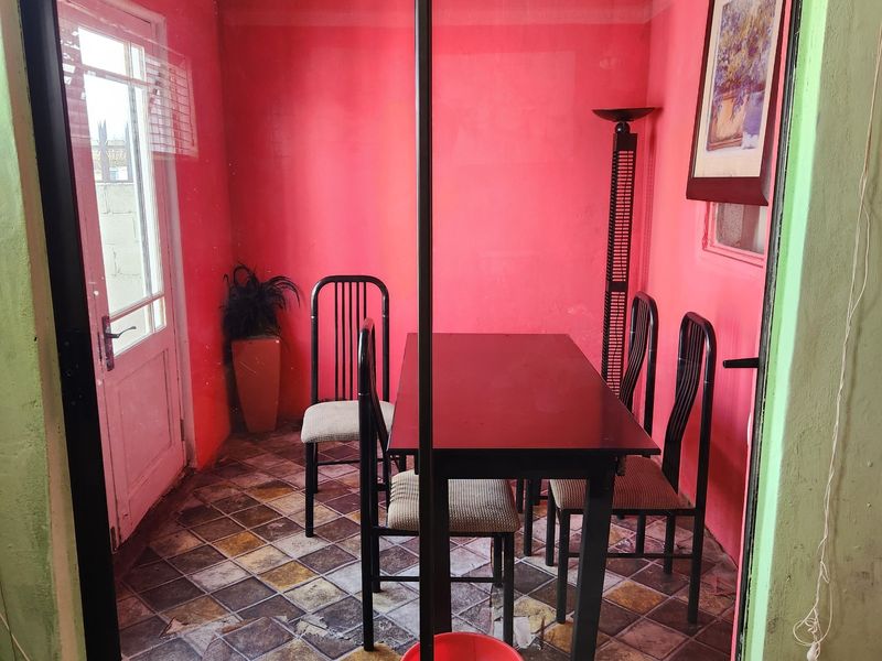 A dining area featuring tiled flooring and a sliding glass door, currently showing significant wear to the wall finishes and floor tiles.