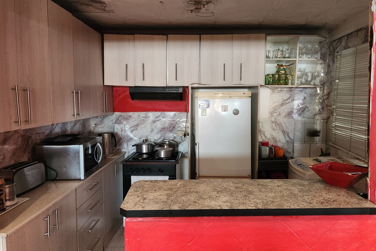 A compact kitchen featuring laminate cabinetry, a breakfast bar, and a marble-effect splashback, currently showing signs of ceiling water damage and general wear.
