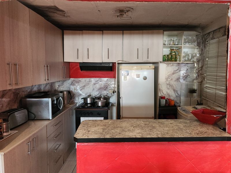 A compact kitchen featuring laminate cabinetry, a breakfast bar, and a marble-effect splashback, currently showing signs of ceiling water damage and general wear.