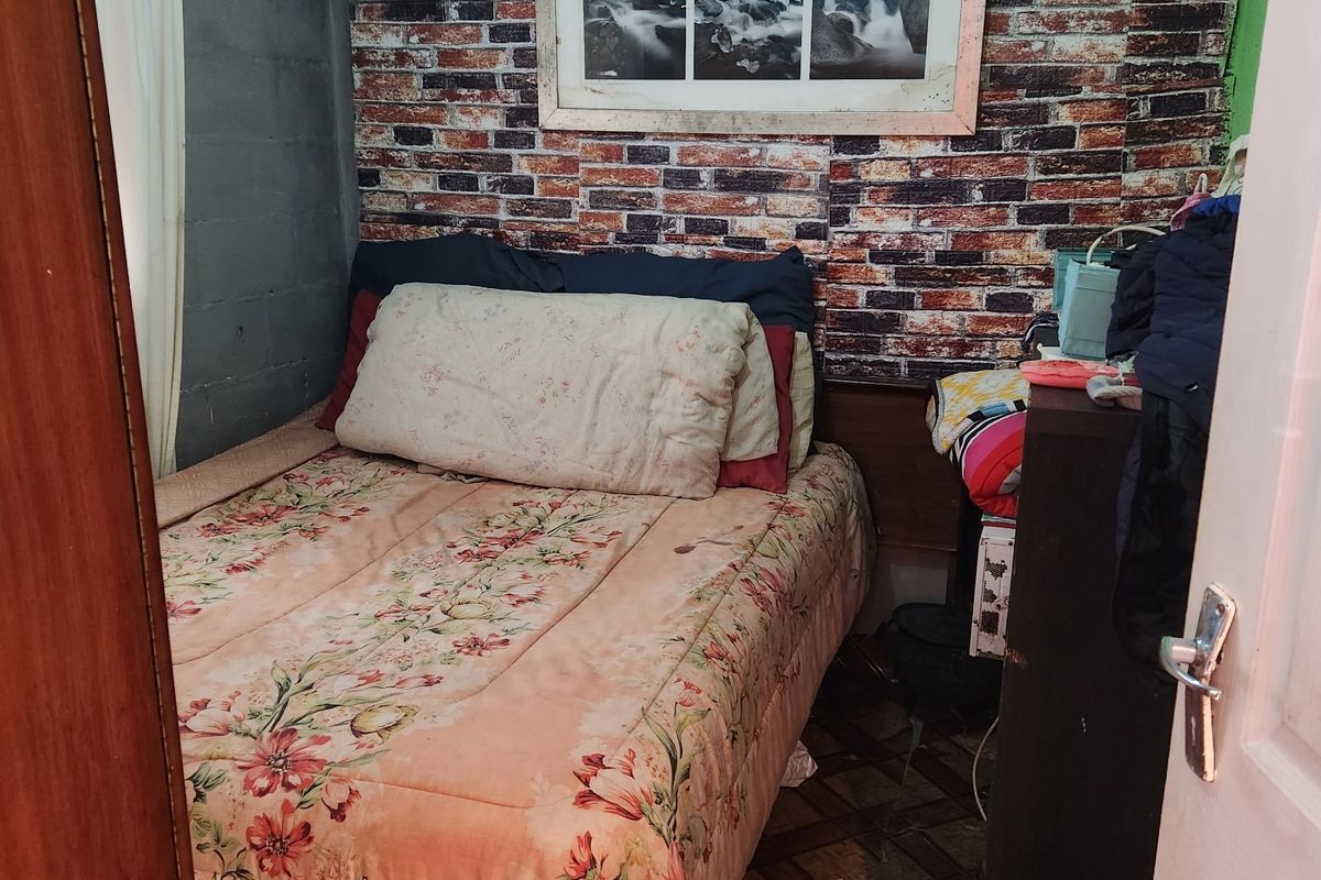 A compact bedroom featuring brick-effect wallpaper, textured ceiling tiles, and tiled flooring, offering a functional space in need of cosmetic updates.