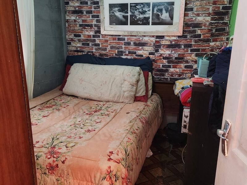 A compact bedroom featuring brick-effect wallpaper, textured ceiling tiles, and tiled flooring, offering a functional space in need of cosmetic updates.