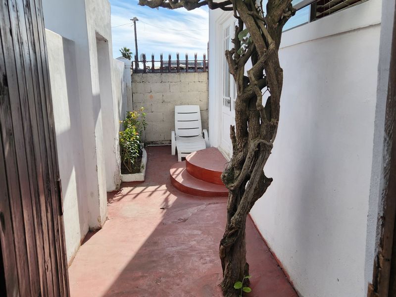 A narrow rear courtyard featuring a paved surface, a raised step, and a boundary wall with security spikes.